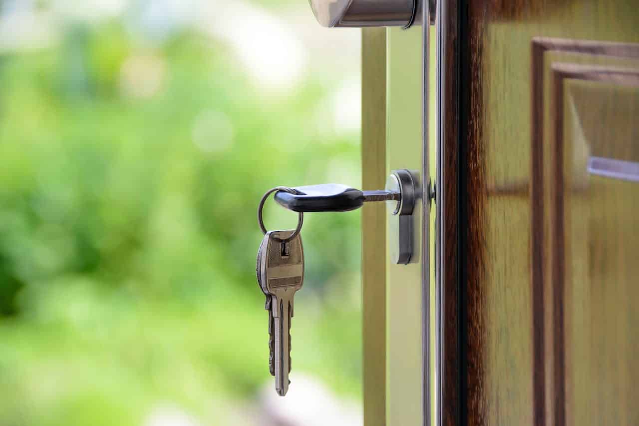 Clé de maison avec porte-clés insérée dans une serrure de porte ouverte, laissant apercevoir un arrière-plan vert et flou.